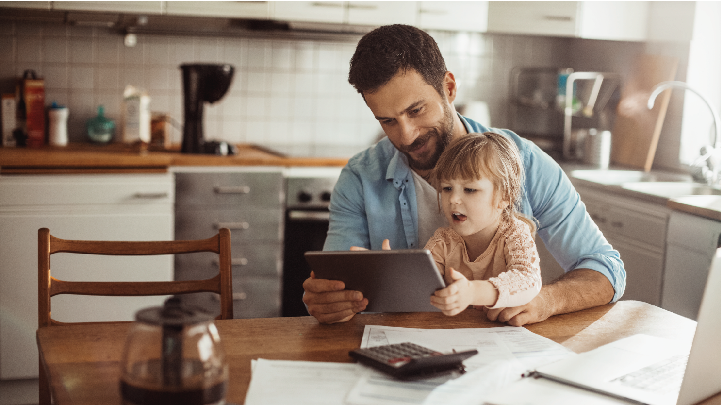 Dad on tablet and kitchen table with young daughter
